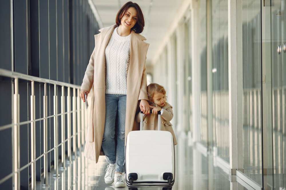 Mãe e filha caminhando com uma mala no corredor do aeroporto